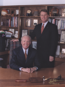 Don O. Walsworth sits at a wood desk while his son, Don Walsworth, stands behind him.