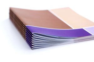 a stack of tan printed books stacked on top of each other with a white background. 