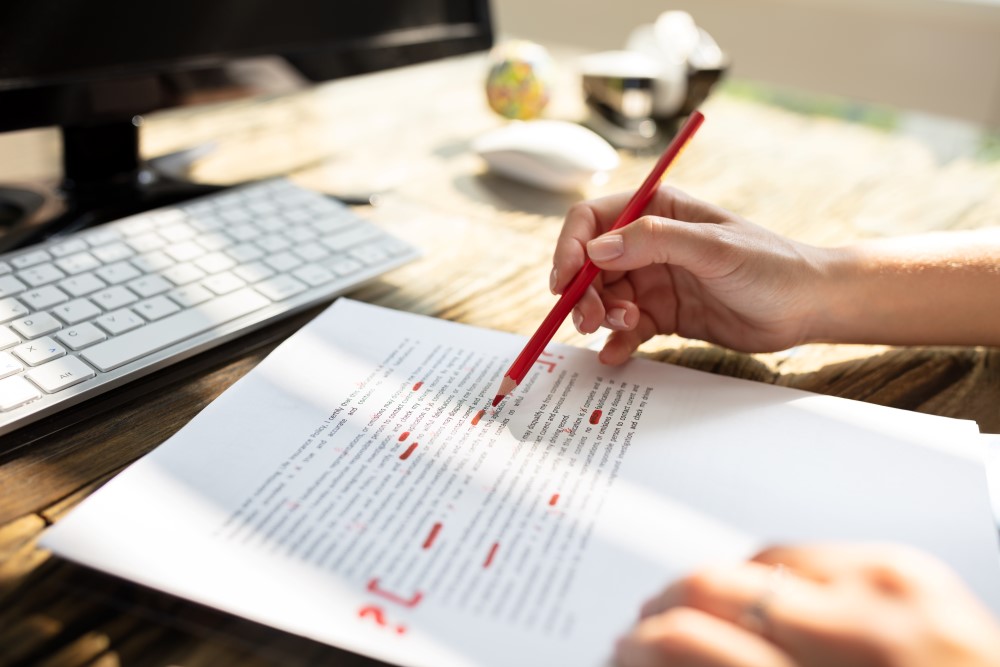 A hand with a red pencil makes corrections to text on a piece of paper