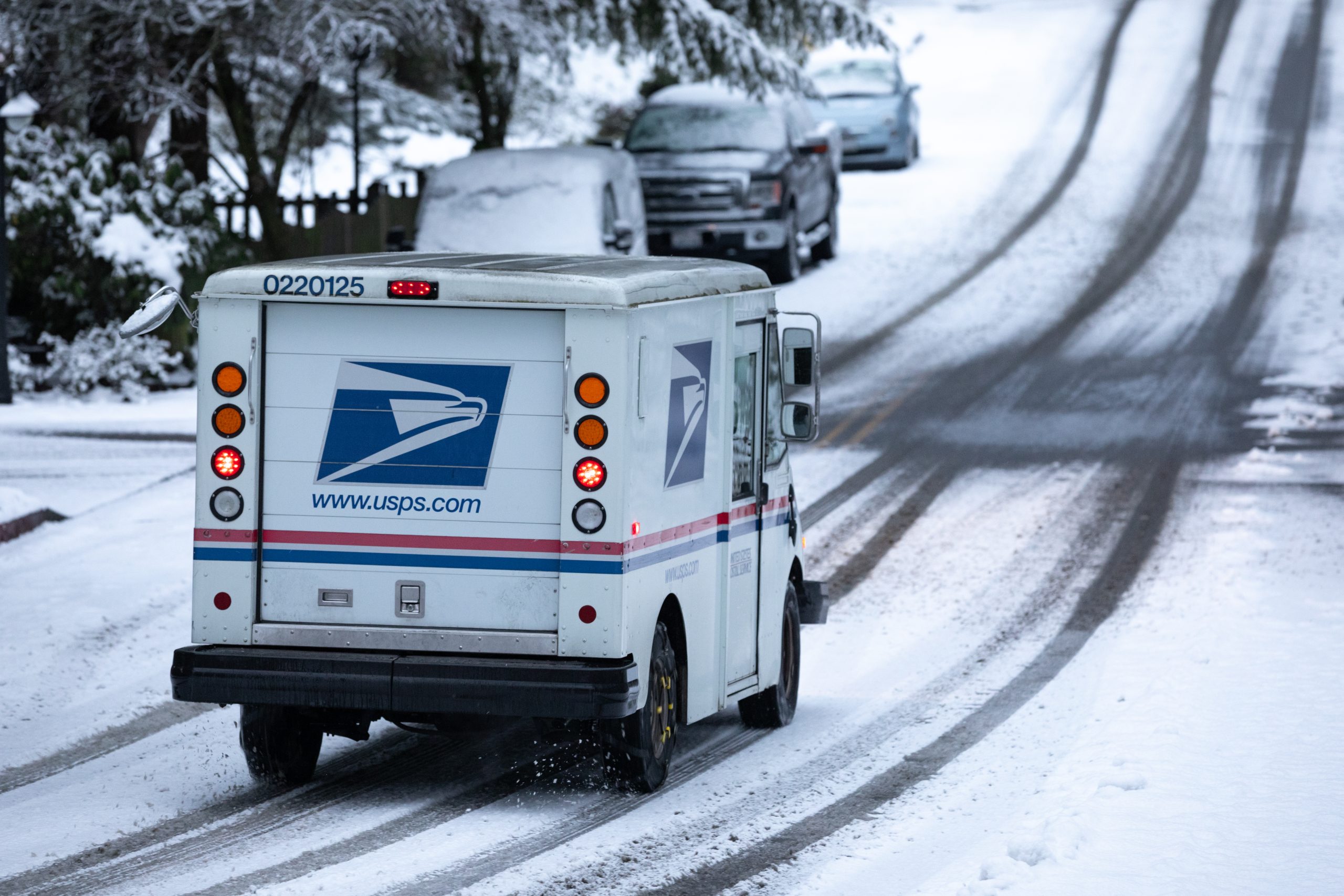 USPS truck driving through a road covered in snow.