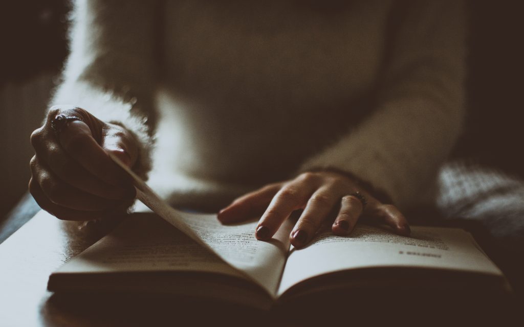 a photograph of someone with a book placed in front of them. They are flipped through pages.