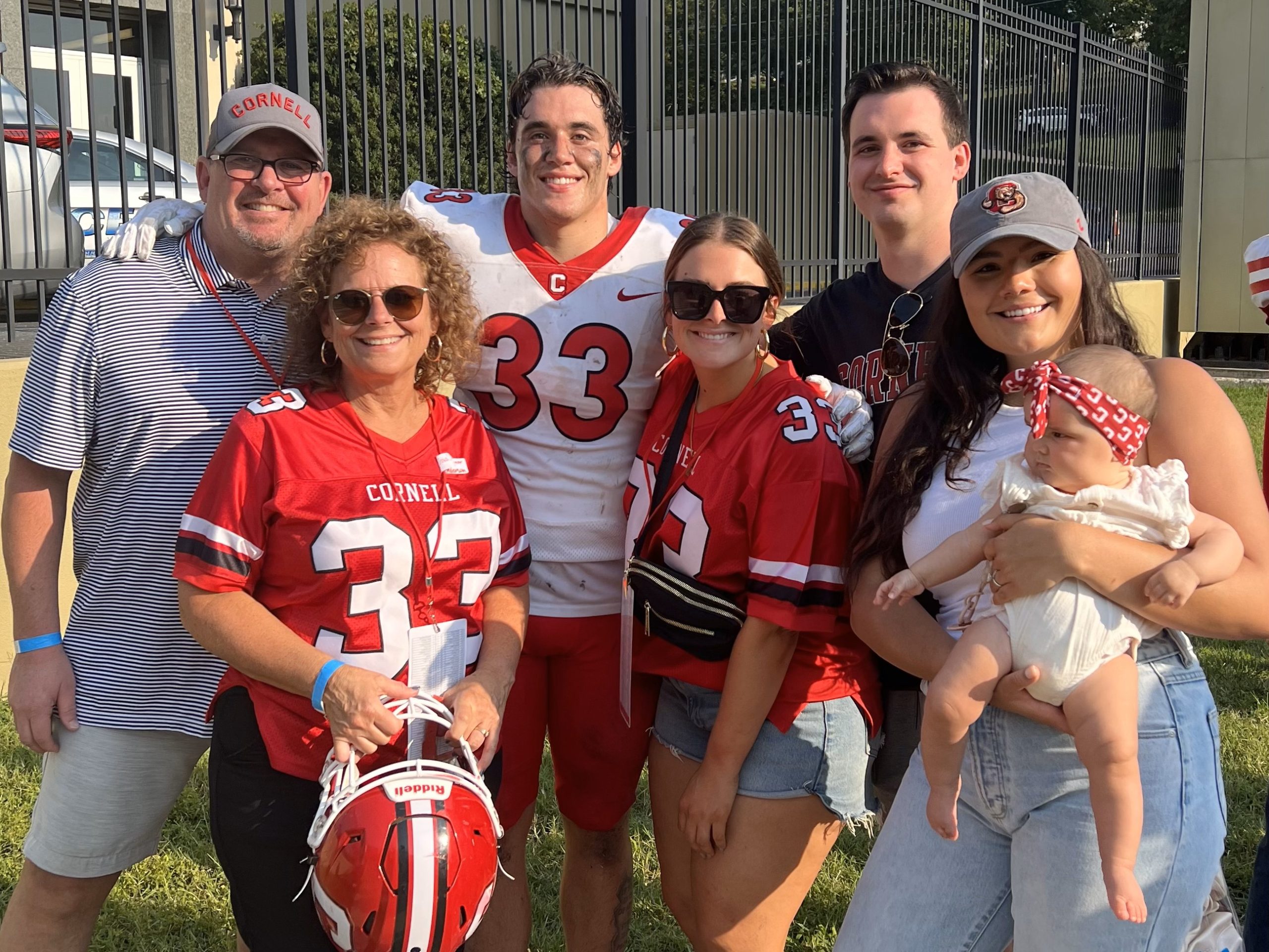 Employee Spotlight Carolyn Henderson. Carolyn wears a Cornell football jersey with the number 33 on it. She is standing next to her husband and son, who is wearing his full Cornell football uniform. Text: “I work with area schools to help them produce the yearbook of their dreams. This means I actively teach in the classroom, educating students and teachers about design, copy writing, photography, marketing, and basically how to run a small business.” Carolyn Henderson, Yearbook Sales Representative, Matthews, North Carolina