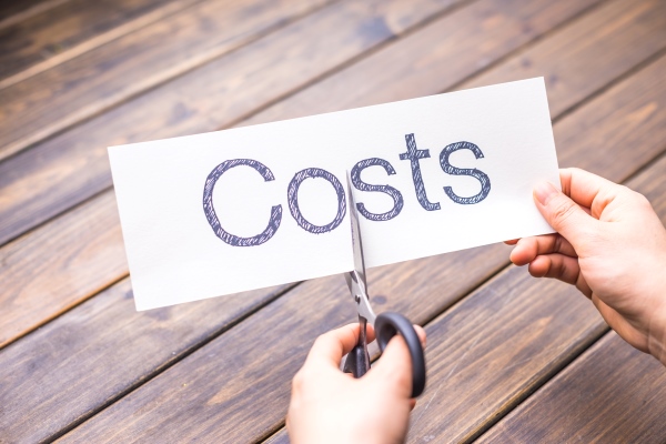Hands holding a pair of scissors, about to cut through a piece of paper that reads "costs"