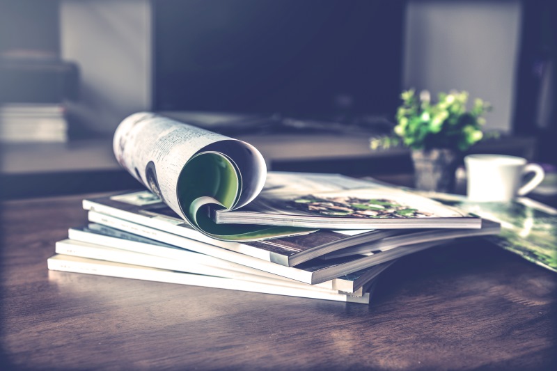 A stack of magazines on a wood table with the top magazine folded open.