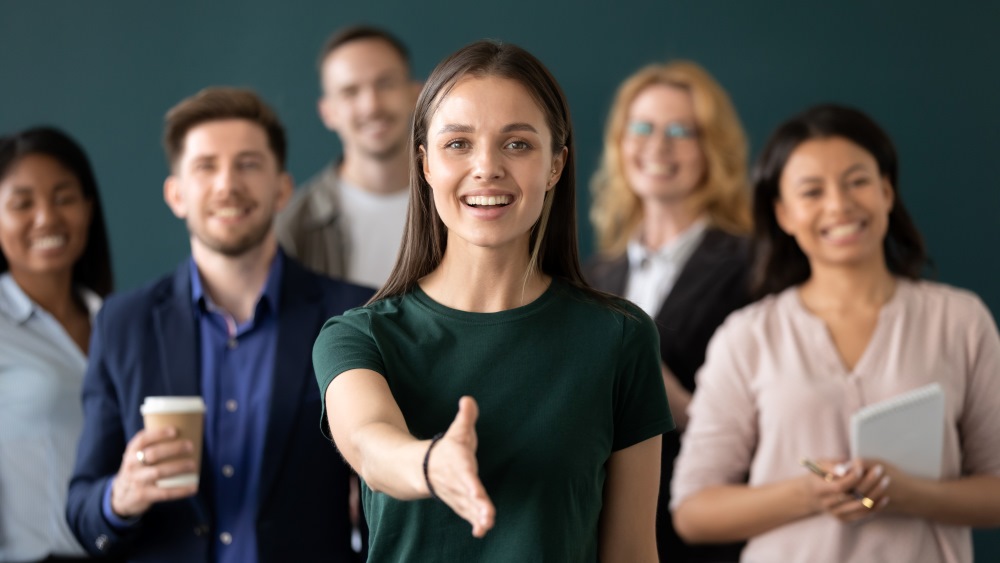 A smiling team of professionals with a young woman in front extending her hand for a handshake