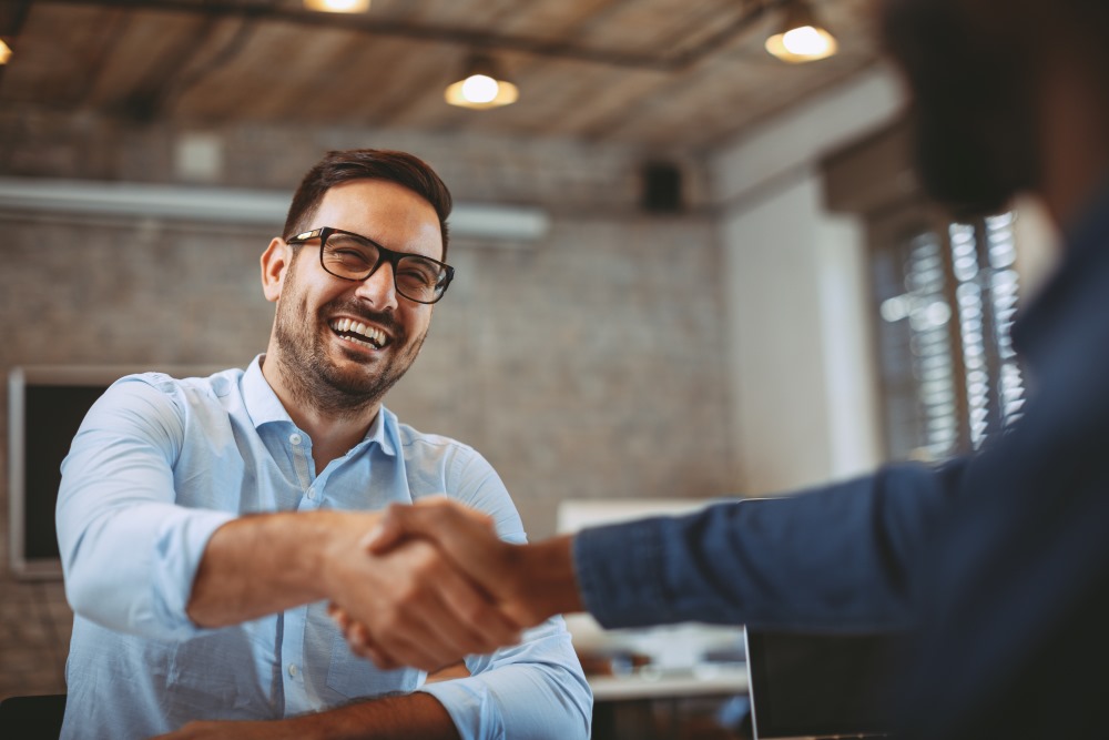 A smiling man in a blue shirt shaking hands with a new business partner