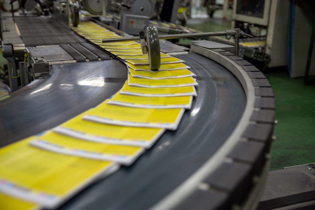 A line of yellow magazine signatures traveling down a printing press