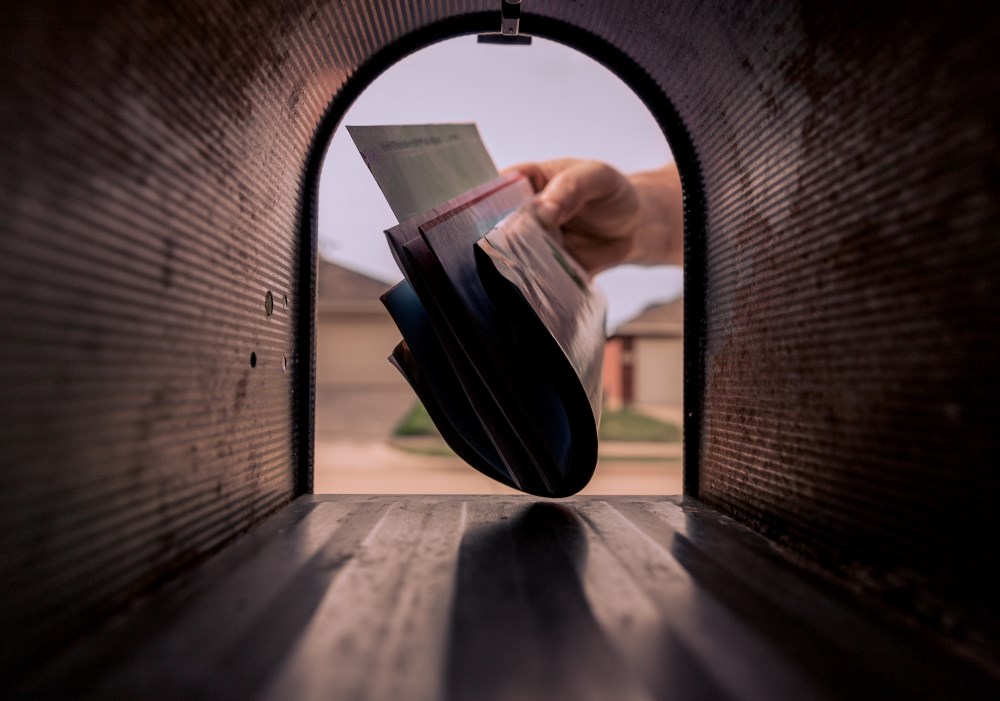 A hand placing a stack of mail into a mailbox