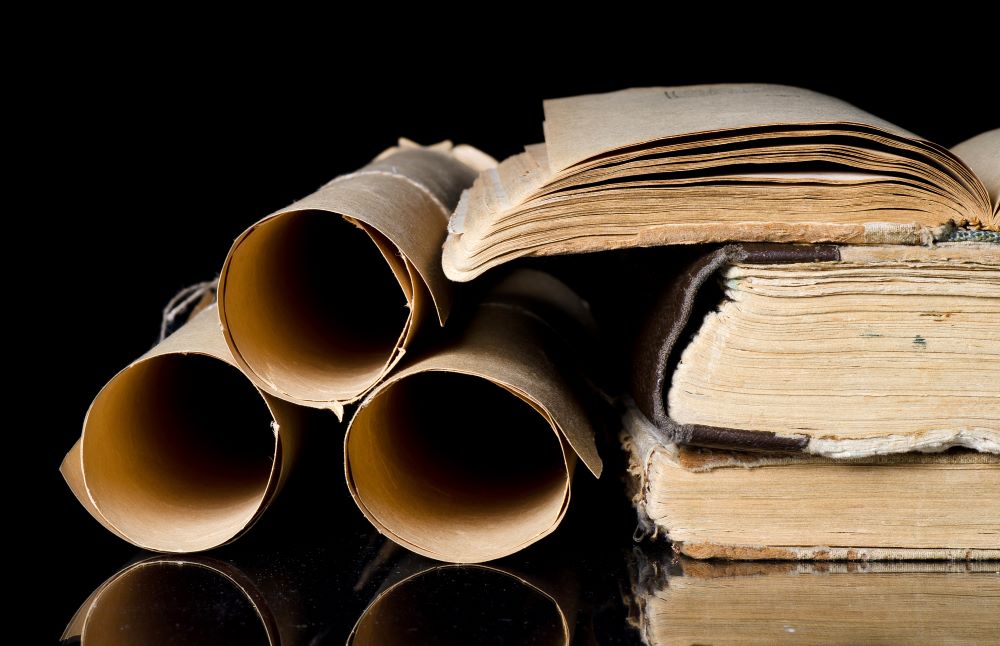 Three scrolls and three old-looking books stacked in front of a black background