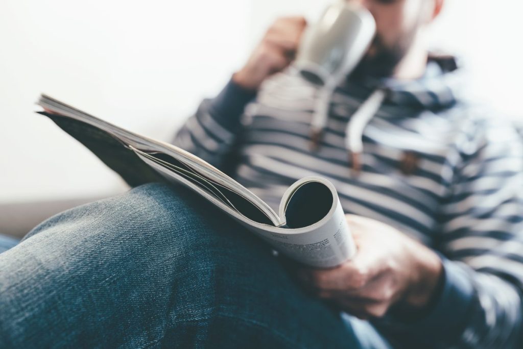 A man sitting on a chair reading a magazine