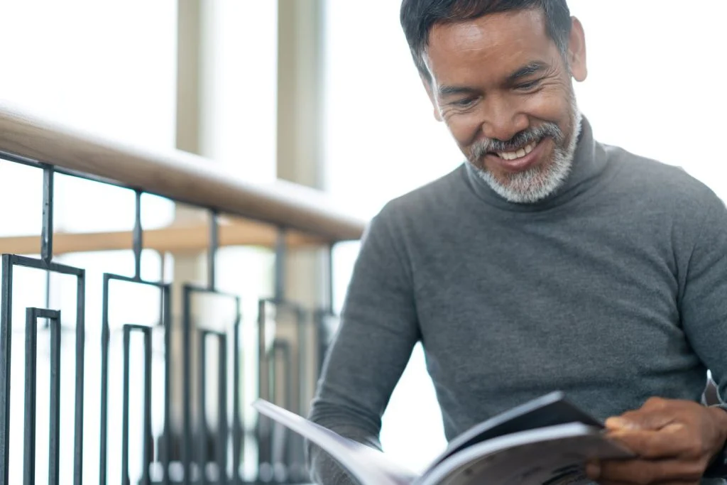 An older man smiling while reading a magazine