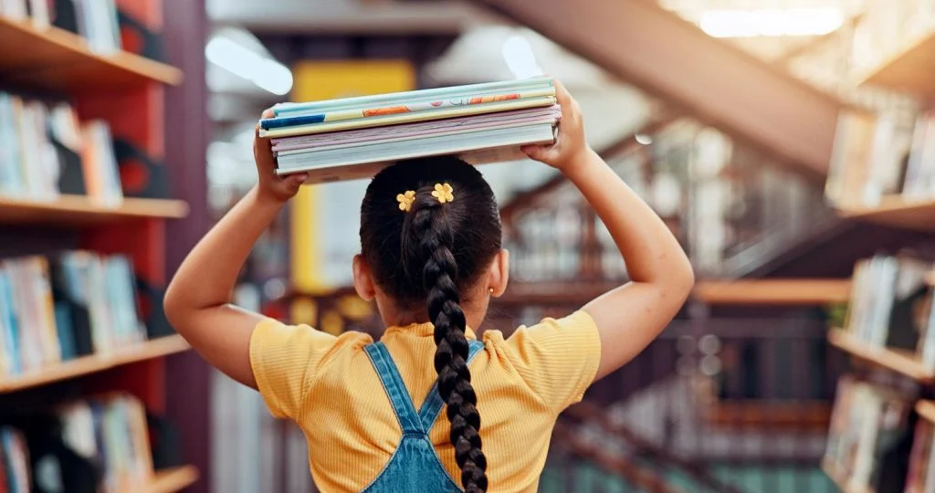 A young girl with a stack of books on her head