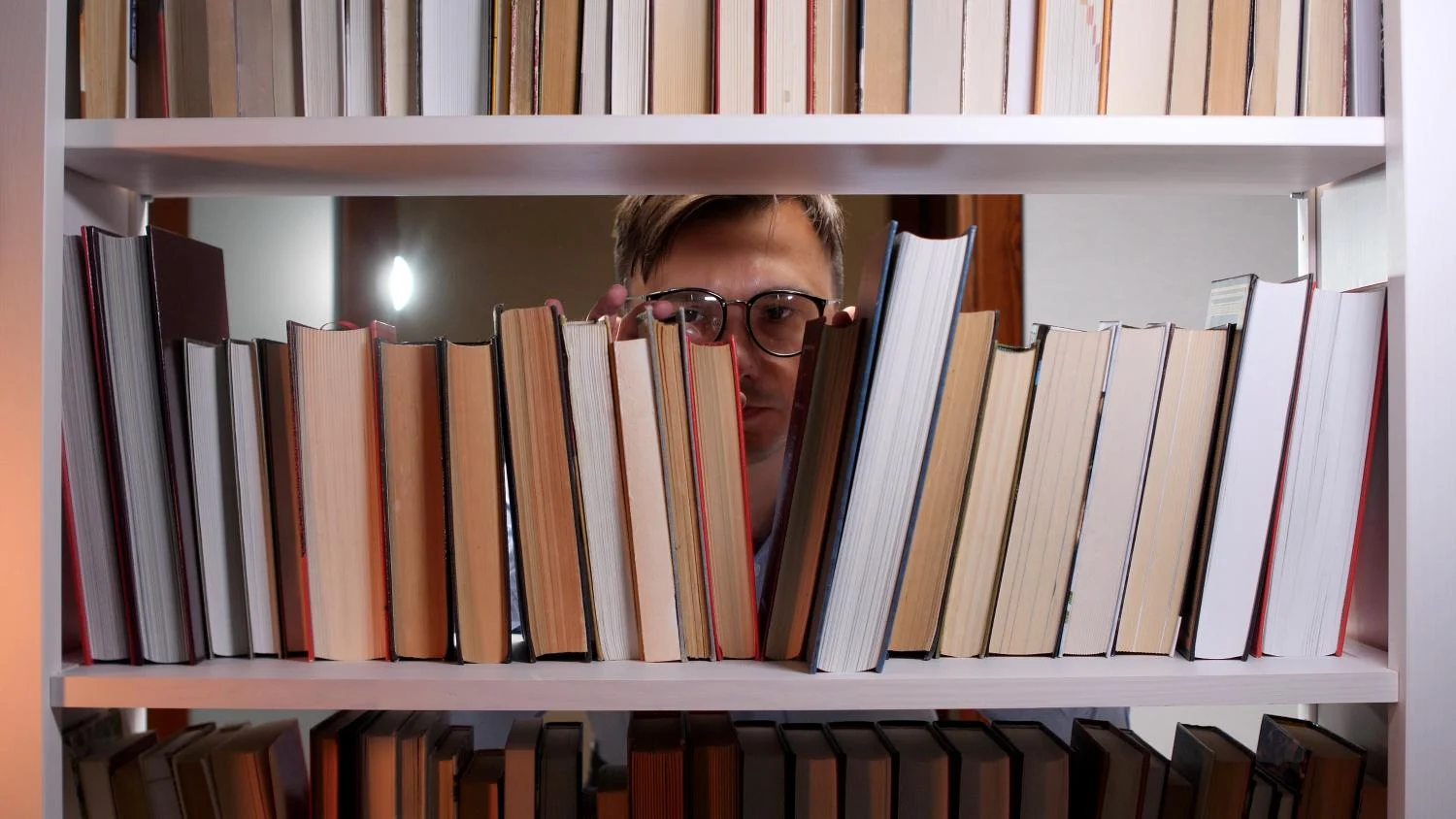 A man wearing glasses perusing books on a shelf