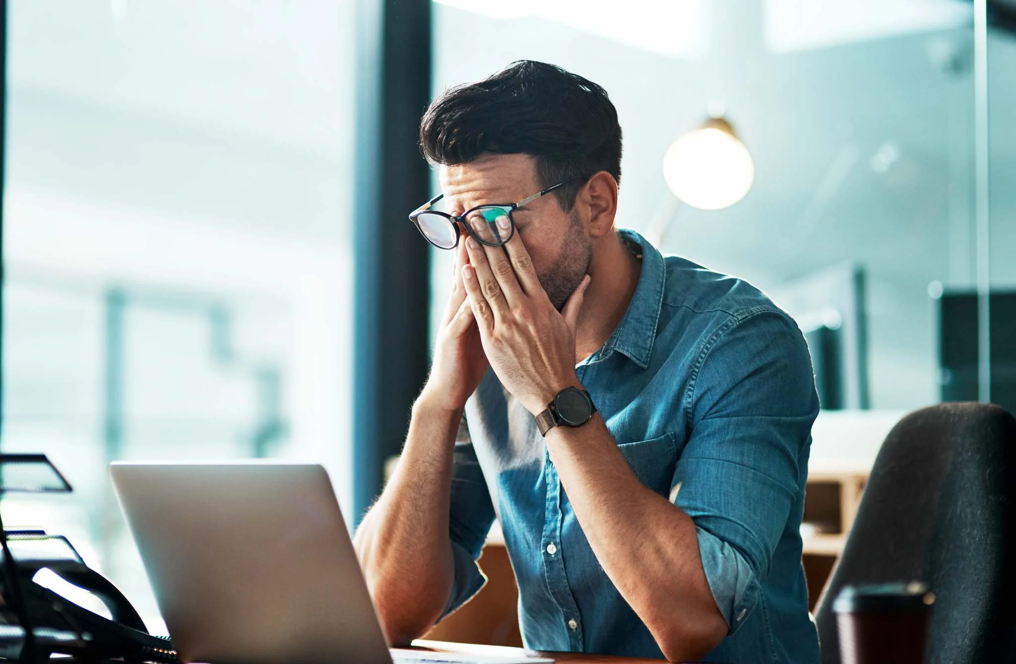 A man sits in front of his laptop rubbing his eyes